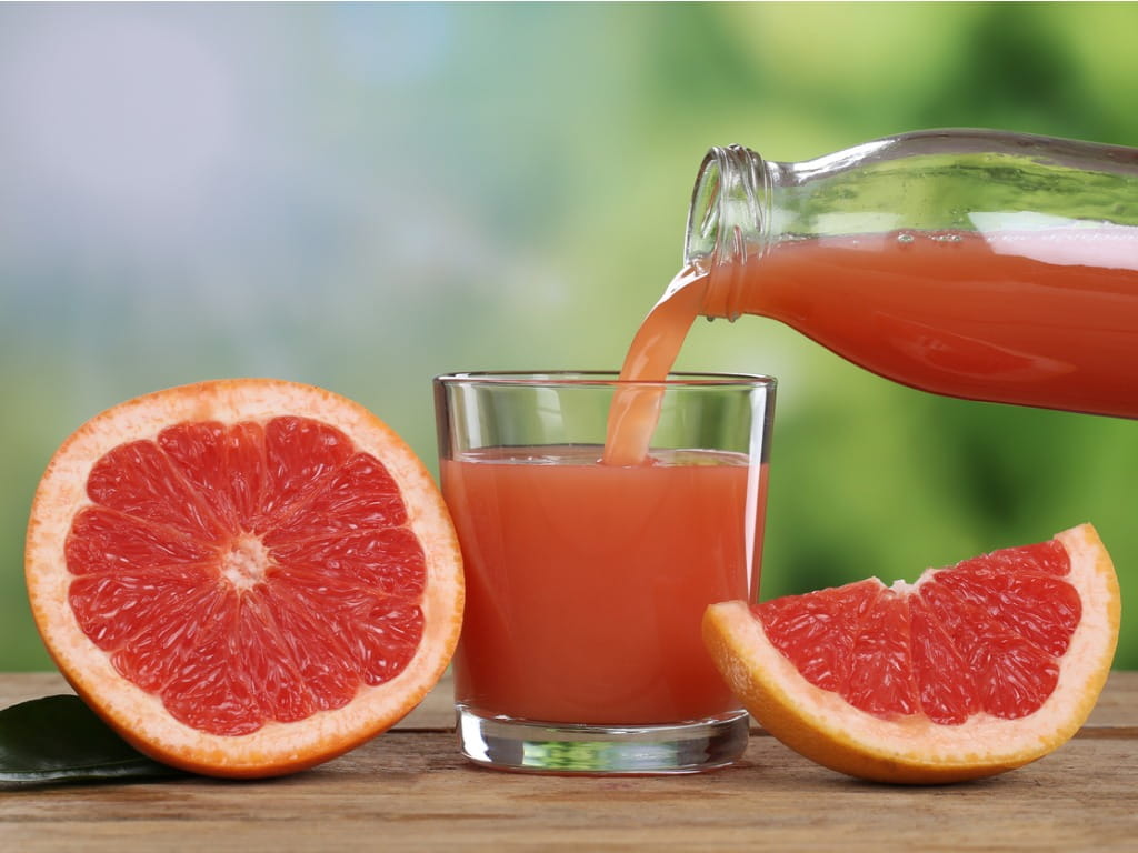 grapefruit juice being poured into a glass next to grapefruits