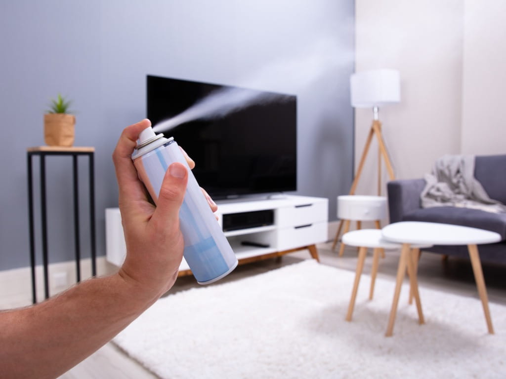 hand spraying air freshener in living room