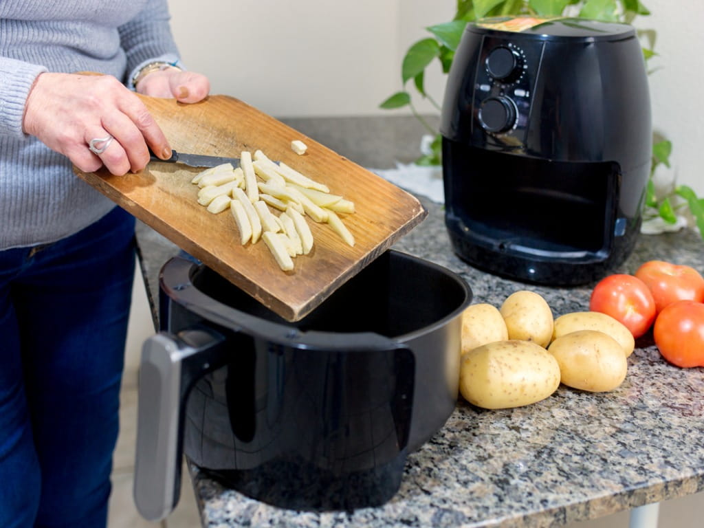 person putting french fries in an air fryer
