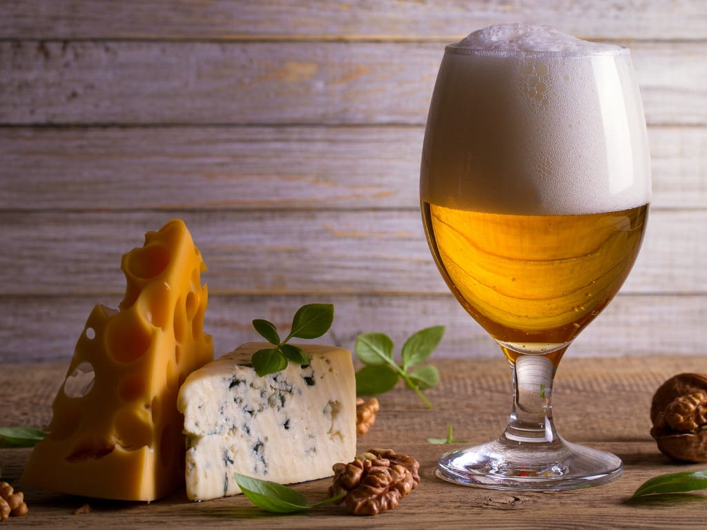 two triangles of cheese next to a glass of beer