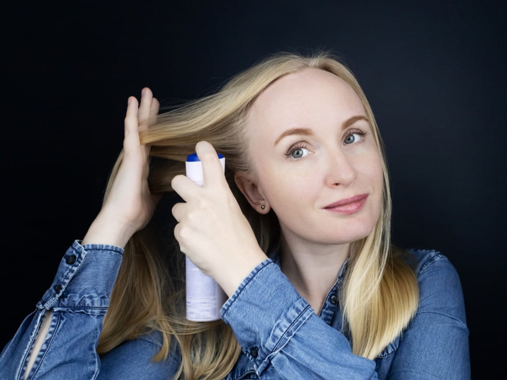 blonde woman using dry shampoo spray