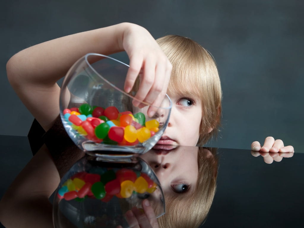 child sticking his hand inside of a candy jar