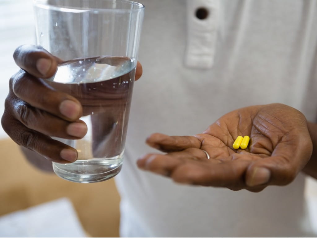 close up of man with yellow capsules in one hand and a glass of water in the other
