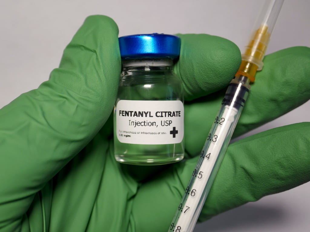 hand holding a bottle of fentanyl and a syringe