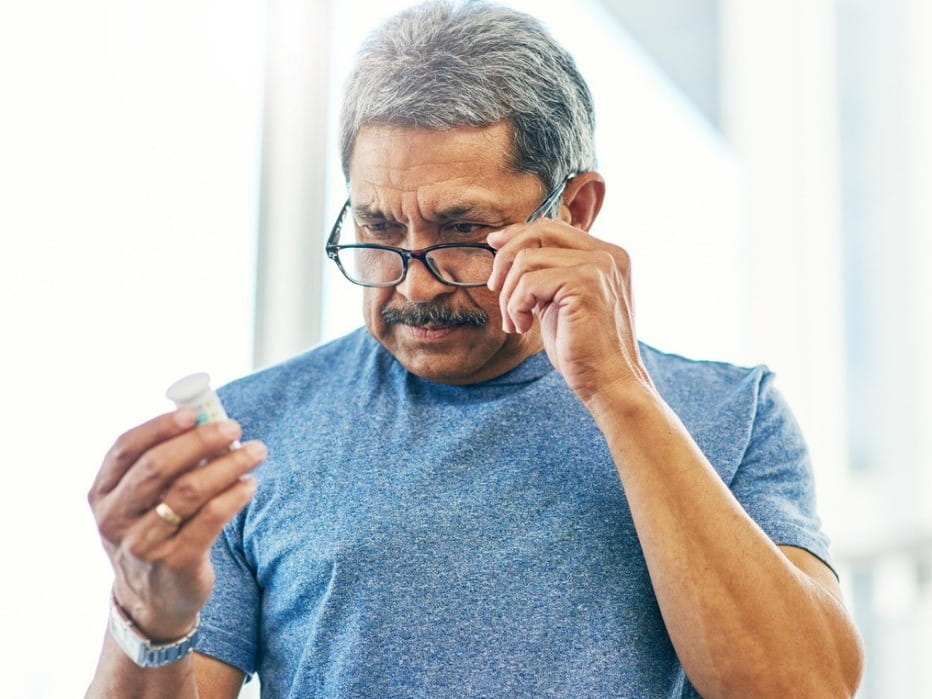 Man using his glasses to read the label on a medicine bottle