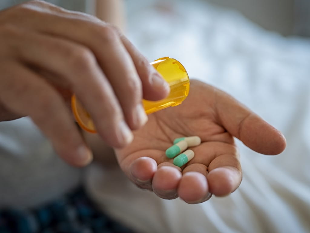 closeup of a man's hand holding a medication bottle and three pills