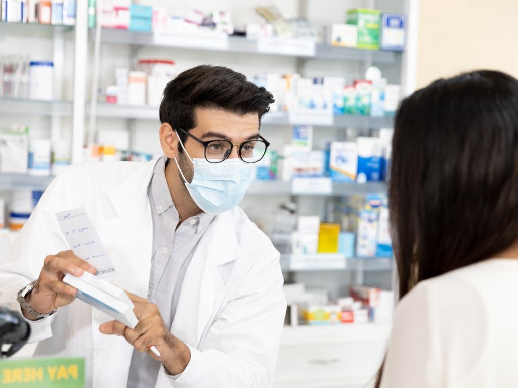 masked pharmacist showing a medication to customer