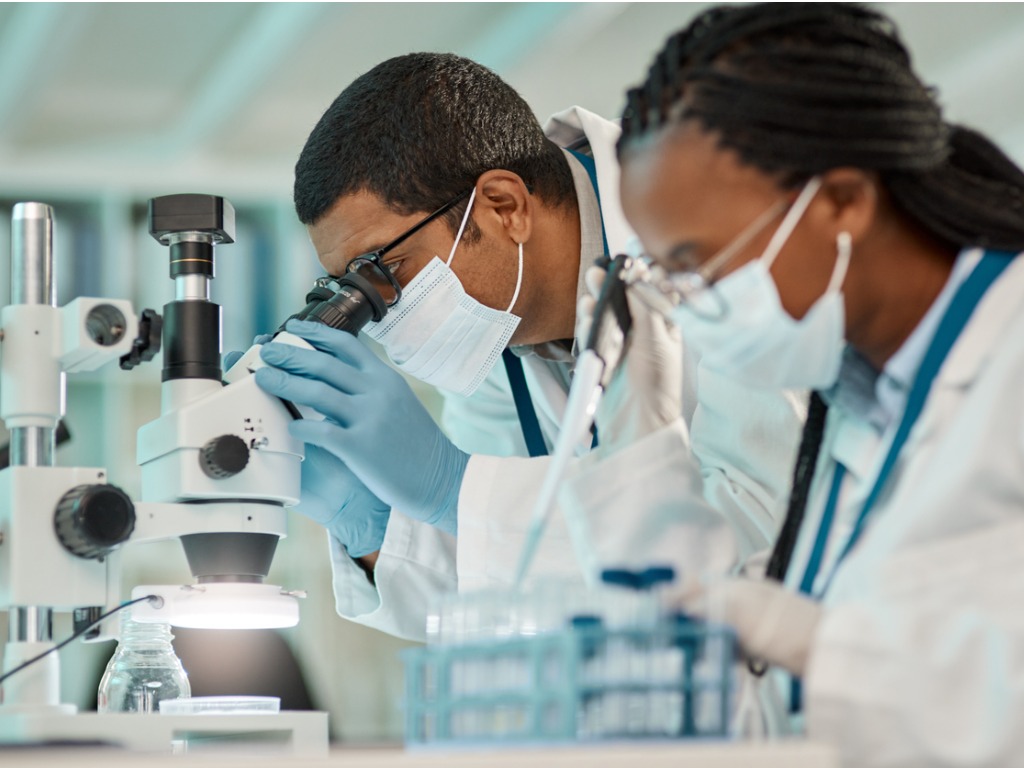 two scientists wearing masks in a lab, looking at microscopes