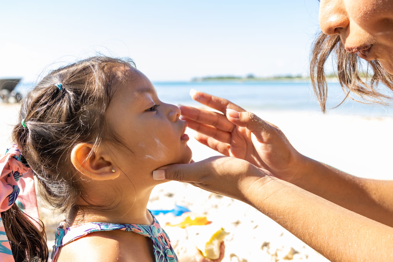 moms rubs sunscreen on daughter's nose at the beach