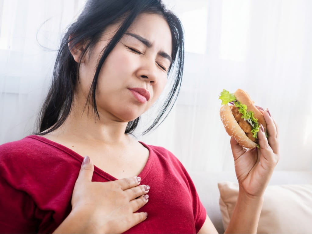 woman having heartburn while holding a burger