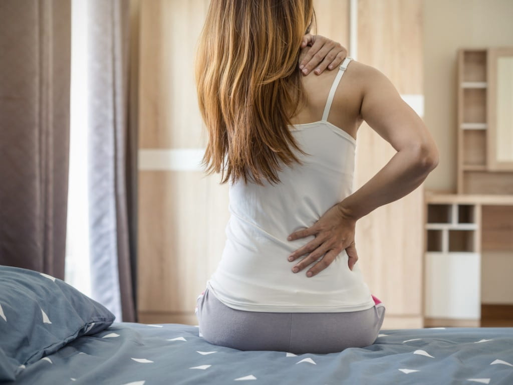 woman sitting on bed with back and shoulder pain 