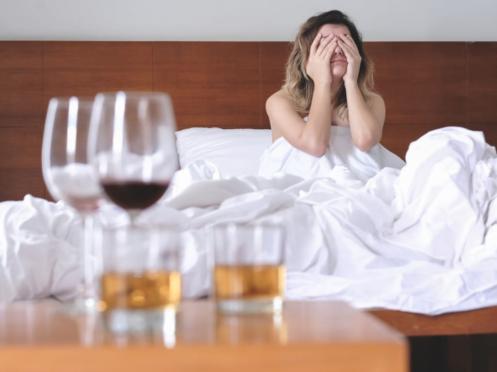 hungover woman in bed next to alcohol