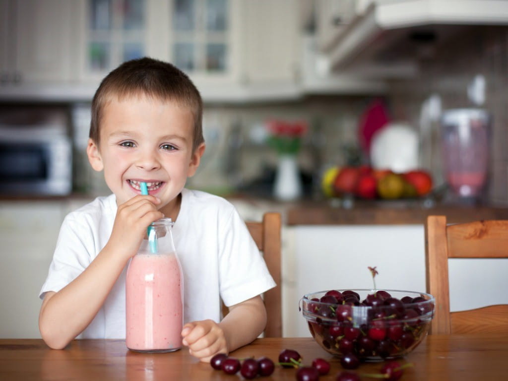 boy drinking cherry smoothie with bowl of cherries on table